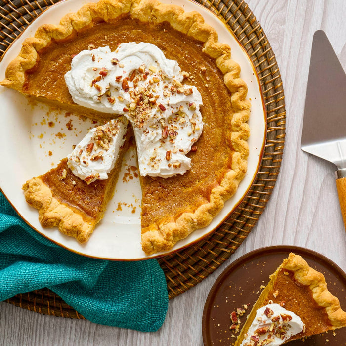 A delicious pumpkin pie topped with whipped cream and pecans sits on a table with a slice already served on a plate.