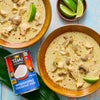 Two bowls of Thai chicken soup with lime wedges are displayed next to a can of Thai Kitchen evaporated coconut milk.