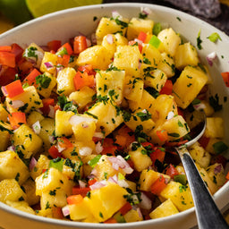 A close-up of a vibrant pineapple salsa in a white bowl, featuring diced pineapple, red bell pepper, red onion, and fresh green herbs, suggesting a dish that could be enhanced by Mccormick Gourmet Cilantro 0.43 Oz.