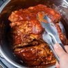 A close-up of a hand using tongs to lift a piece of meat out of a pot.