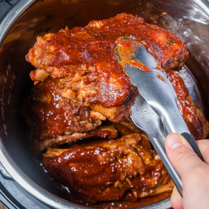 A close-up of a hand using tongs to lift a piece of meat out of a pot.