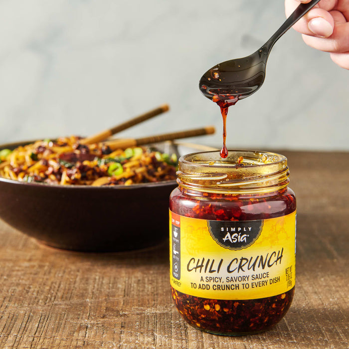 A jar of Simply Asia Chili Crunch sauce with a spoon dripping sauce over the top.