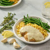 A plate of chicken with a creamy sauce, rice, and green beans.