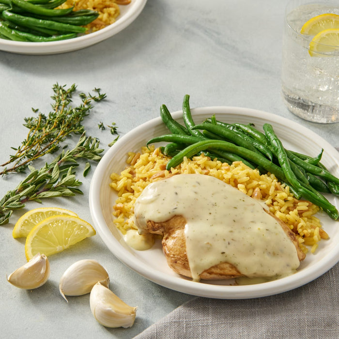 A plate of chicken with a creamy sauce, rice, and green beans.