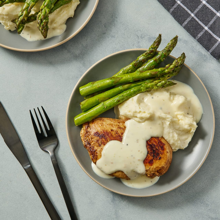 A plate of chicken, mashed potatoes, and asparagus with a creamy sauce.