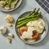 A plate of chicken, mashed potatoes, asparagus, and white sauce.