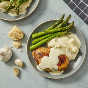 A plate of chicken, mashed potatoes, asparagus, and white sauce.