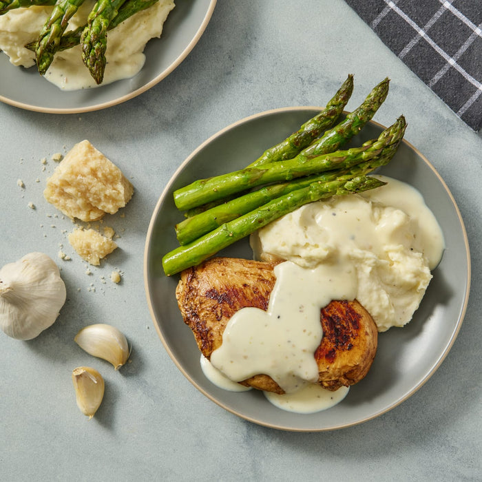 A plate of chicken, mashed potatoes, asparagus, and white sauce.