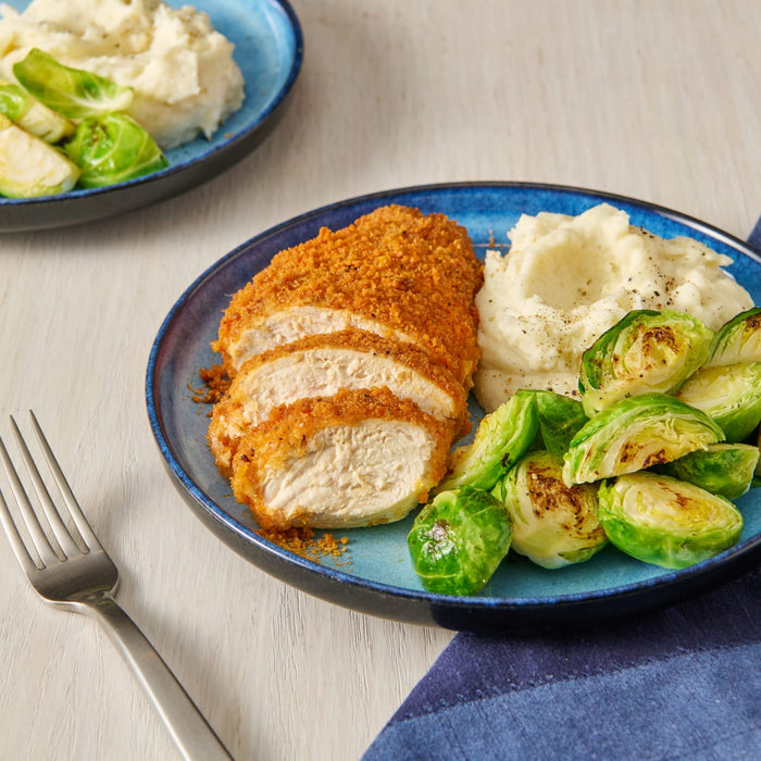 A plate of breaded chicken, mashed potatoes, and brussel sprouts.