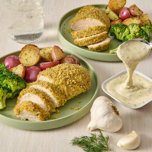 A plate of breaded chicken with roasted potatoes and broccoli, with a side of creamy sauce.