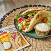 McCormick Shawarma Pita with Garlic Sauce seasoning packet and a plate of pita bread filled with chicken, vegetables, and a side of sauce.