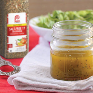 A glass jar of salt-free salad dressing sits on a white cloth next to a container of salt-free seasoning.