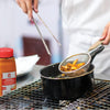 A chef is using tongs to lift a strainer full of french fries out of a pot of hot oil.
