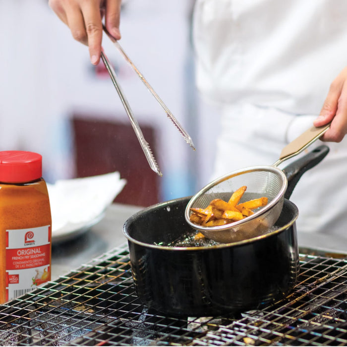 A chef is using tongs to lift a strainer full of french fries out of a pot of hot oil.