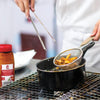 A chef is using tongs to remove french fries from a pot of hot oil.