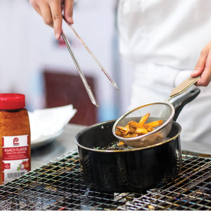 A chef is using tongs to remove french fries from a pot of hot oil.