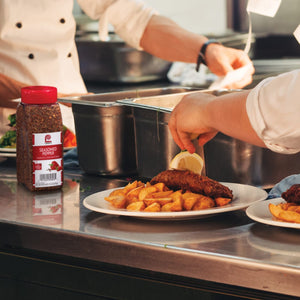 A chef is preparing a plate of food with a lemon wedge on top, next to a bottle of Lawry's Seasoned Pepper.