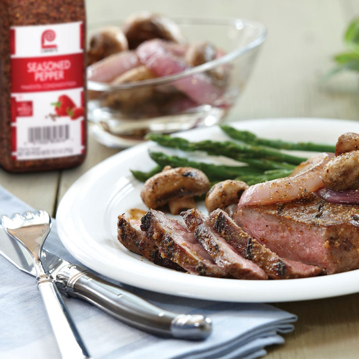 A plate of sliced steak with asparagus, mushrooms, and red onions, with a bottle of McCormick Seasoned Pepper in the background.