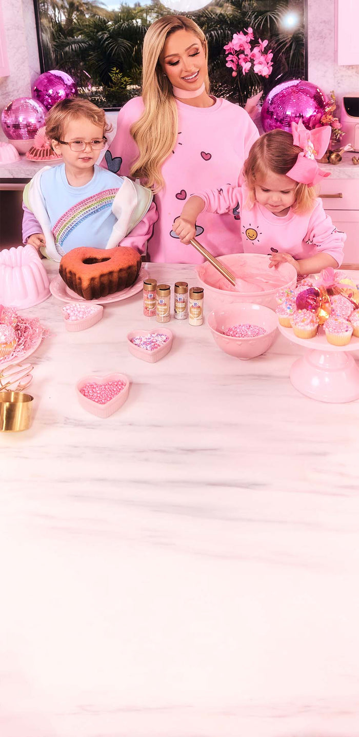 Paris Hilton and two children in the kitchen with pink decorations and a cake.