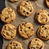 A close-up of nine chocolate chip cookies on a brown parchment paper.