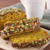 Slices of pumpkin bread with pumpkin seeds on top are on a wooden cutting board.