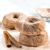 Three cinnamon sugar donuts are stacked on top of each other with cinnamon sticks on the side.