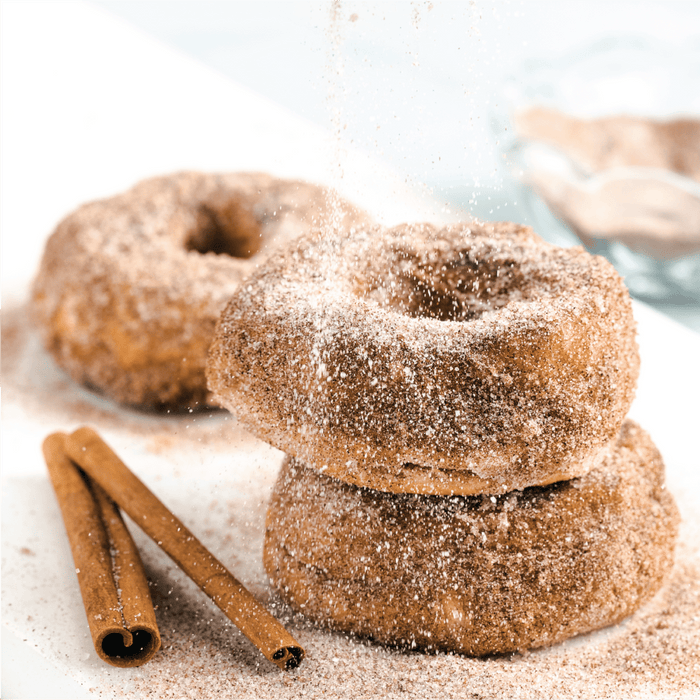 Three cinnamon sugar donuts are stacked on top of each other with cinnamon sticks on the side.