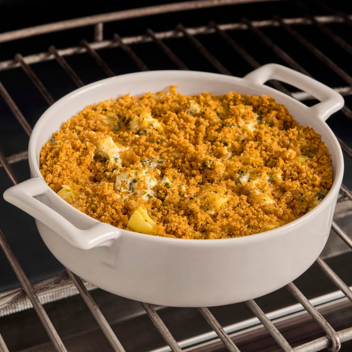 A white casserole dish filled with a cheesy breadcrumb-topped dish sits on a wire rack in an oven.