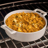 A white casserole dish filled with a cheesy breadcrumb-topped dish sits on a wire rack in an oven.