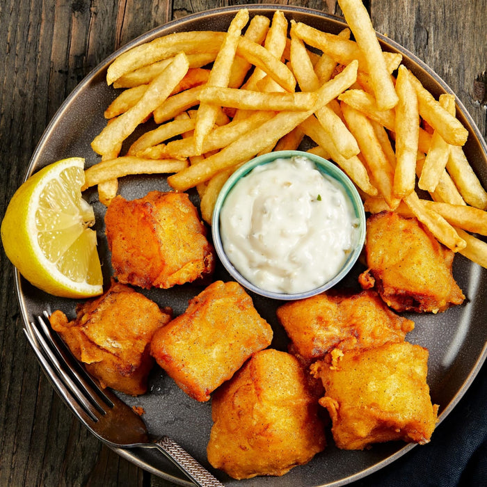 A plate of fish and chips with tartar sauce and a lemon wedge.