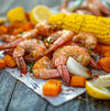 A close-up of a plate of cooked shrimp with corn on the cob squash and onions.
