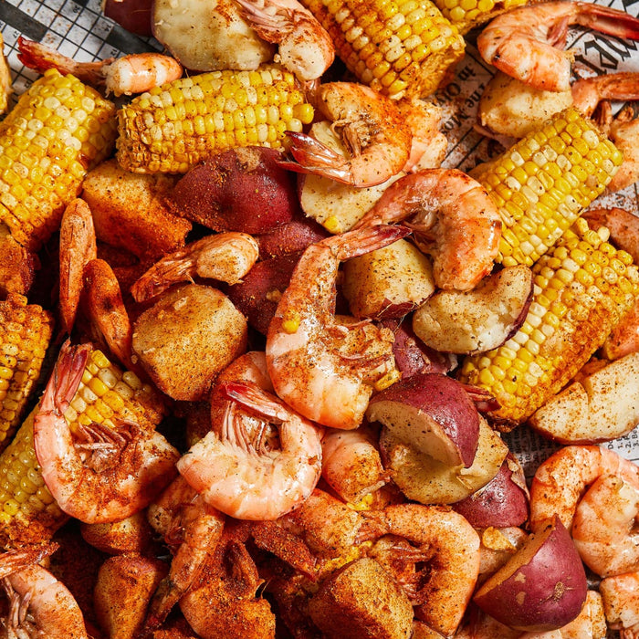 A close-up of a plate of boiled shrimp corn on the cob and red potatoes.