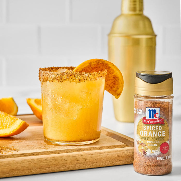 A refreshing cocktail featuring McCormick Spiced Gravy mix as a rim garnish, alongside orange slices and a golden cocktail shaker.