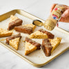 A hand sprinkles McCormick Cinnamon Sugar Blend on chocolate-dipped shortbread cookies on a baking sheet.