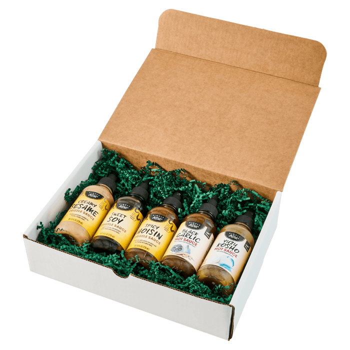 A gift box containing five bottles of various hot sauces nestled in green packaging material.
