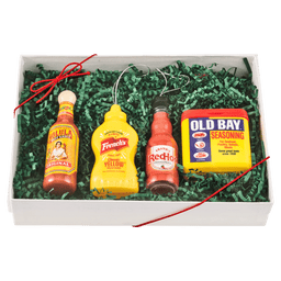 A gift box featuring Old Bay seasoning, Frank's RedHot sauce, French's mustard, and Texas Pete hot sauce, arranged on green decorative filler.