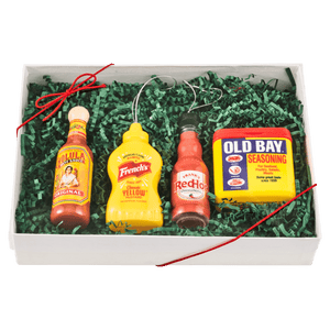 A gift box featuring Old Bay seasoning, Frank's RedHot sauce, French's mustard, and Texas Pete hot sauce, arranged on green decorative filler.
