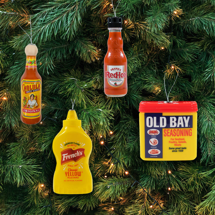 A Christmas tree is decorated with novelty ornaments shaped like bottles of Cholula hot sauce, Frank's RedHot sauce, French's mustard, and a container of Old Bay seasoning.