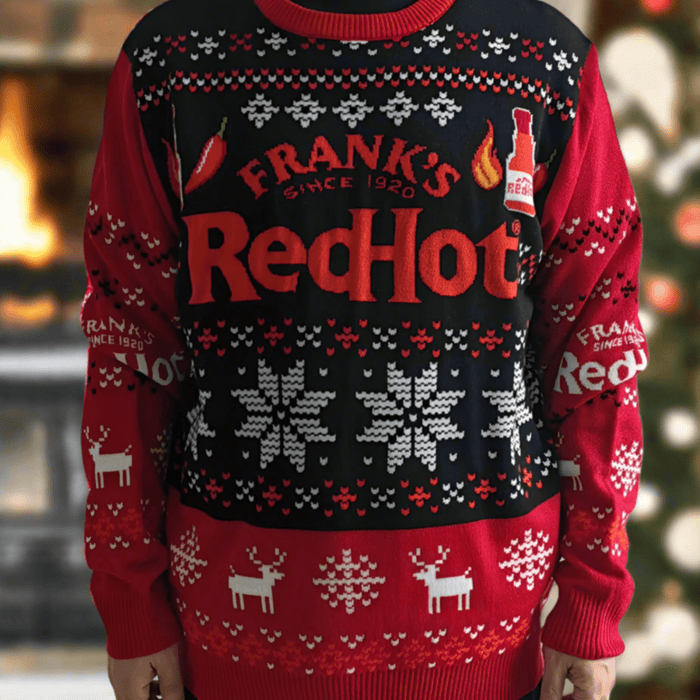 A person wearing a Frank's RedHot ugly Christmas sweater with snowflakes, reindeer, and chili pepper designs.