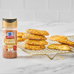 A bottle of McCormick Spiced Orange seasoning sits next to a stack of spiced orange cookies on a gold wire rack.