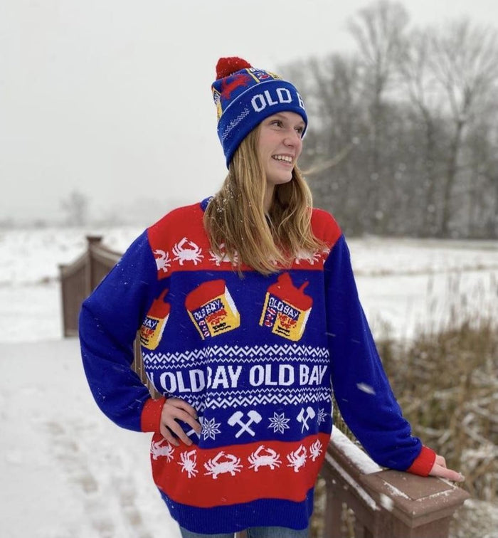 A person wearing an Old Bay themed sweater and hat stands in a snowy landscape.