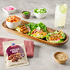 A packet of McCormick Korean BBQ seasoning mix is displayed next to a wooden tray of Korean BBQ lettuce wraps kimchi and other toppings.
