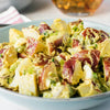 A bowl of red potato salad with a creamy yellow dressing, garnished with green onions.