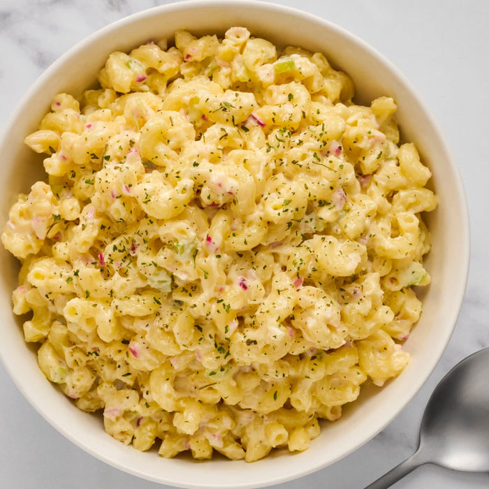 A bowl of creamy macaroni salad with visible bits of celery and red onion, garnished with herbs.