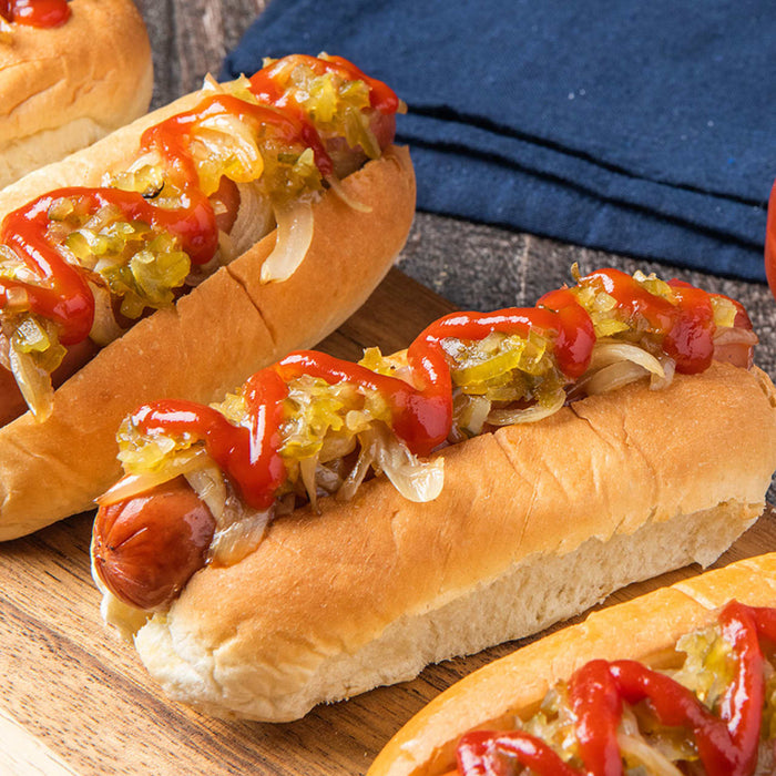 Three hot dogs on buns are topped with ketchup, relish, and onions, showcasing a classic American meal.