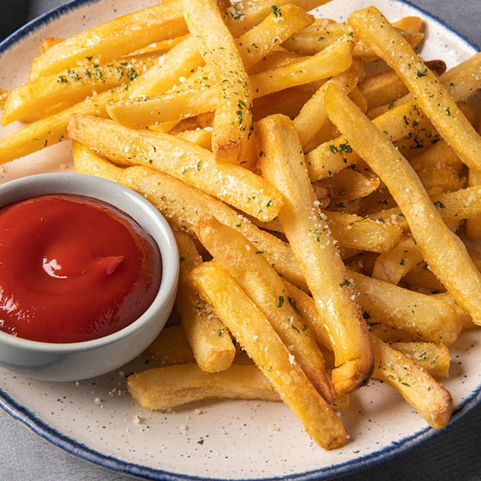 A plate of golden french fries sprinkled with herbs, served with a side of ketchup.