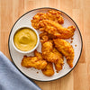 A plate of crispy chicken tenders served with a side of mustard sauce.