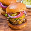 A delicious burger with cheese, tomato, red onion, and pickles on a toasted bun sits on a wooden board.