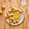 A plate of pigs in a blanket is served with mustard for dipping.