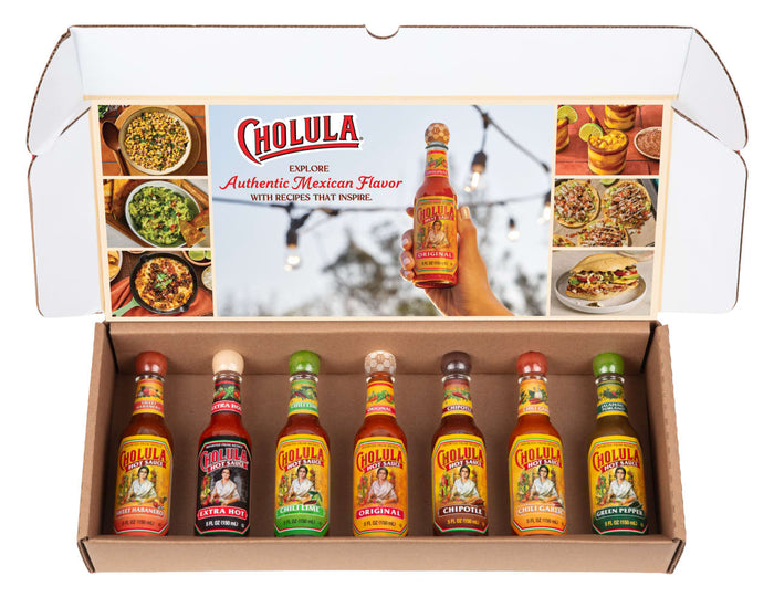 A Cholula Hot Sauce Variety Pack Gift Set is displayed in an open box, showcasing seven different flavors: Sweet Habanero, Extra Hot, Chili Lime, Original, Chipotle, Chili Garlic, and Green Pepper.